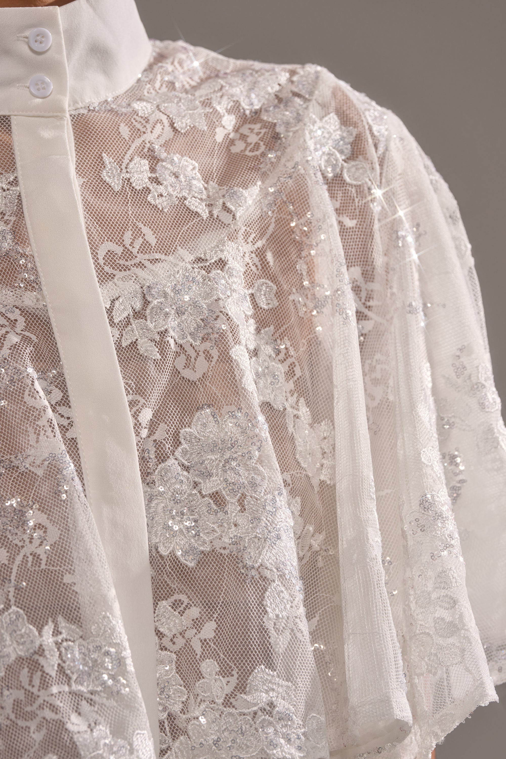 Close-up of the EVA LACE SHORT SLEEVE BUTTON DOWN, showcasing sheer floral mesh with sequin accents, a white collar and buttons, plus elegant embroidery for a delicate finish. 7