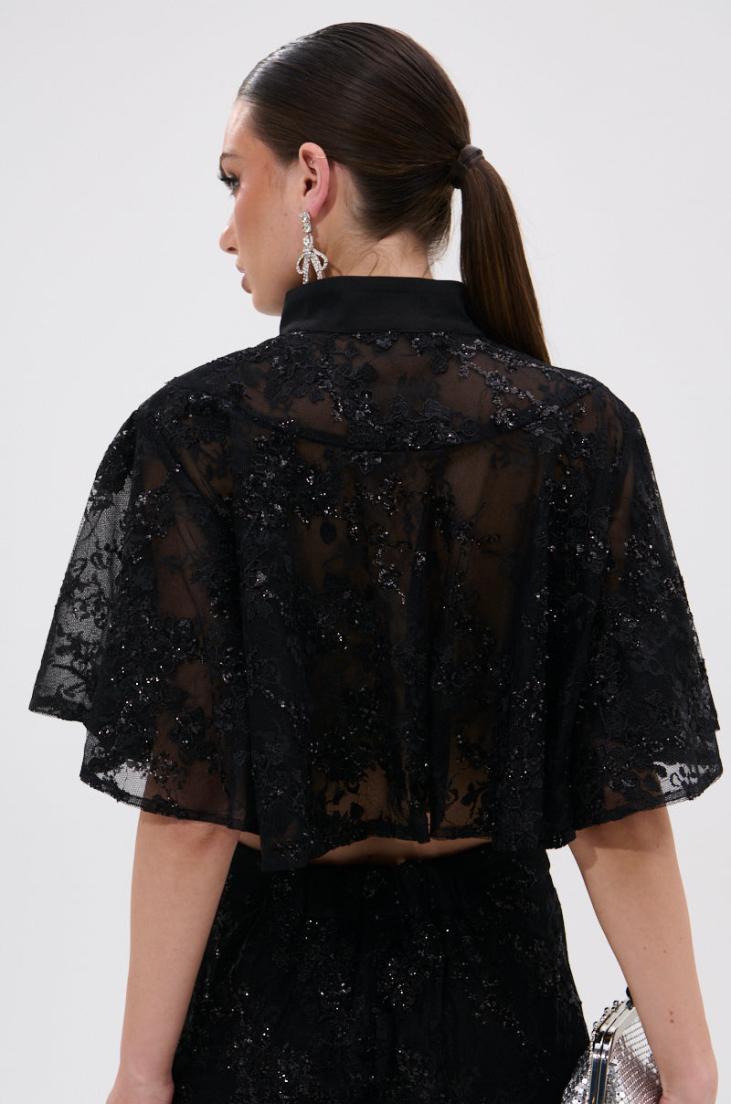 A woman with long brown hair in a low ponytail is seen from the back, wearing the QUEEN B LACE BUTTON DOWN over a matching outfit, accessorized with a small silver purse and dangling earrings.