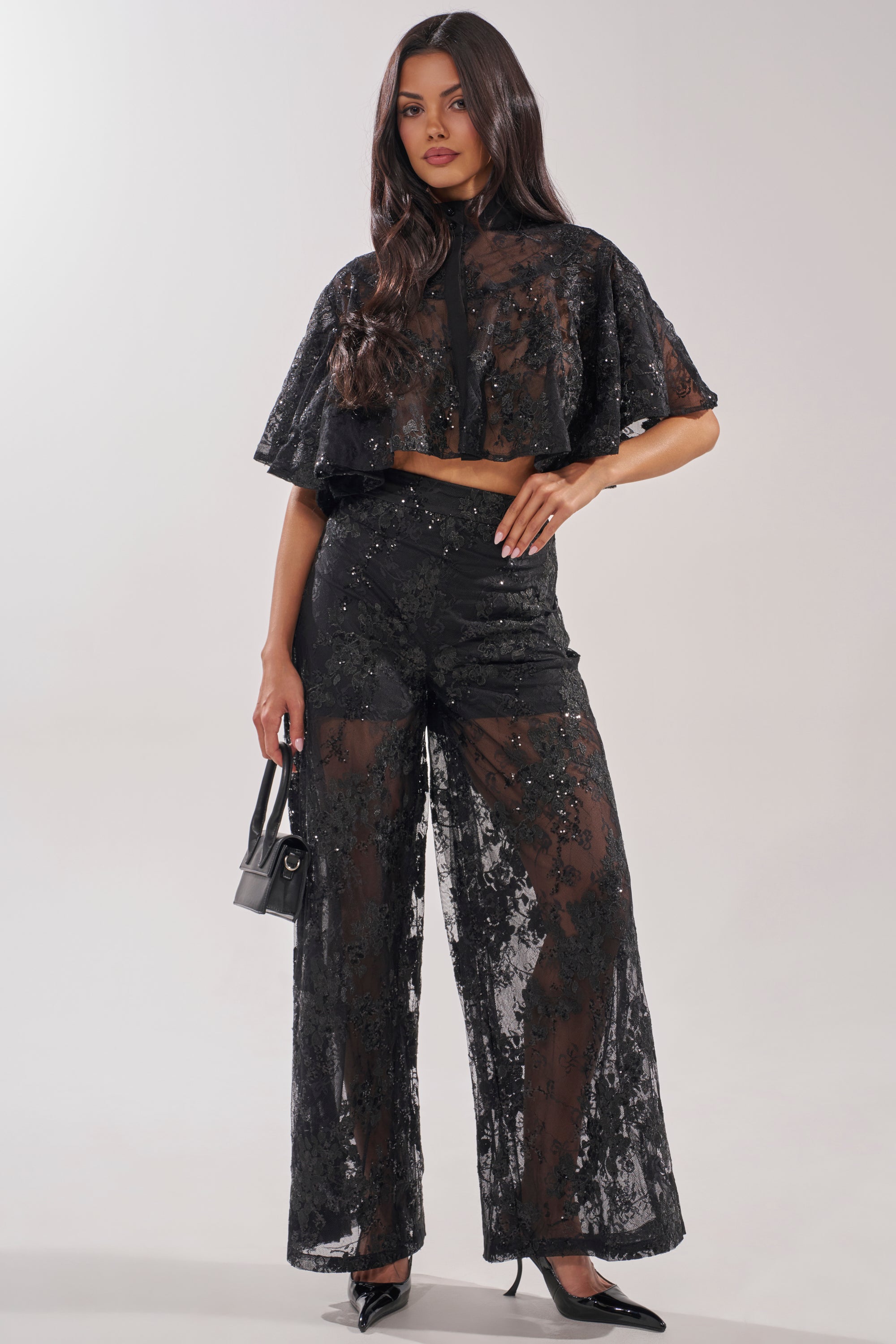 Woman wearing the QUEEN B LACE BUTTON DOWN with wide-leg pants, black heels, and a small black handbag, standing against a plain light background. 5