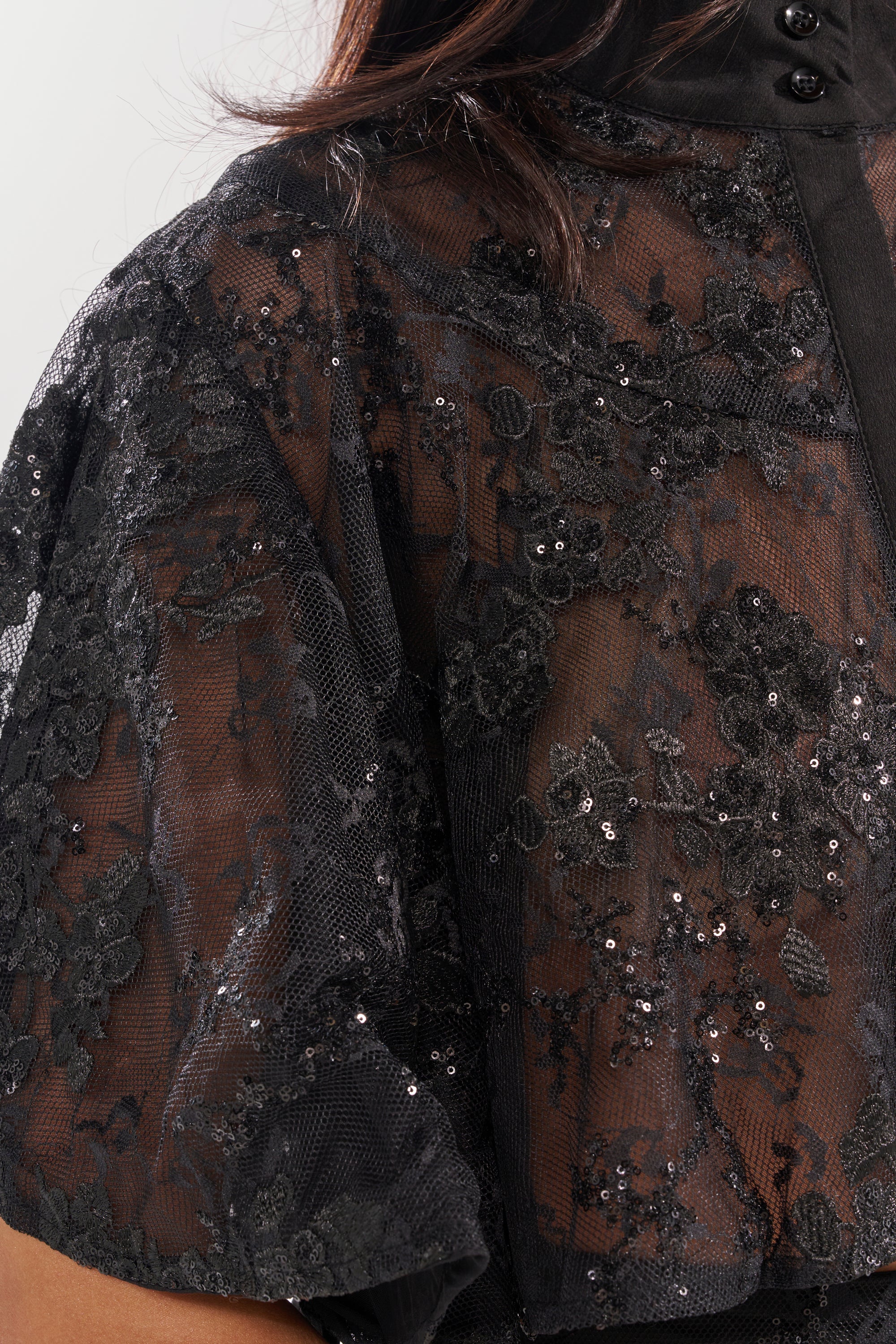 Close-up of the QUEEN B LACE BUTTON DOWN: a sheer floral mesh fabric with sparkling sequin details and intricate florals, slightly transparent and elegantly layered over skin with short sleeves. 6