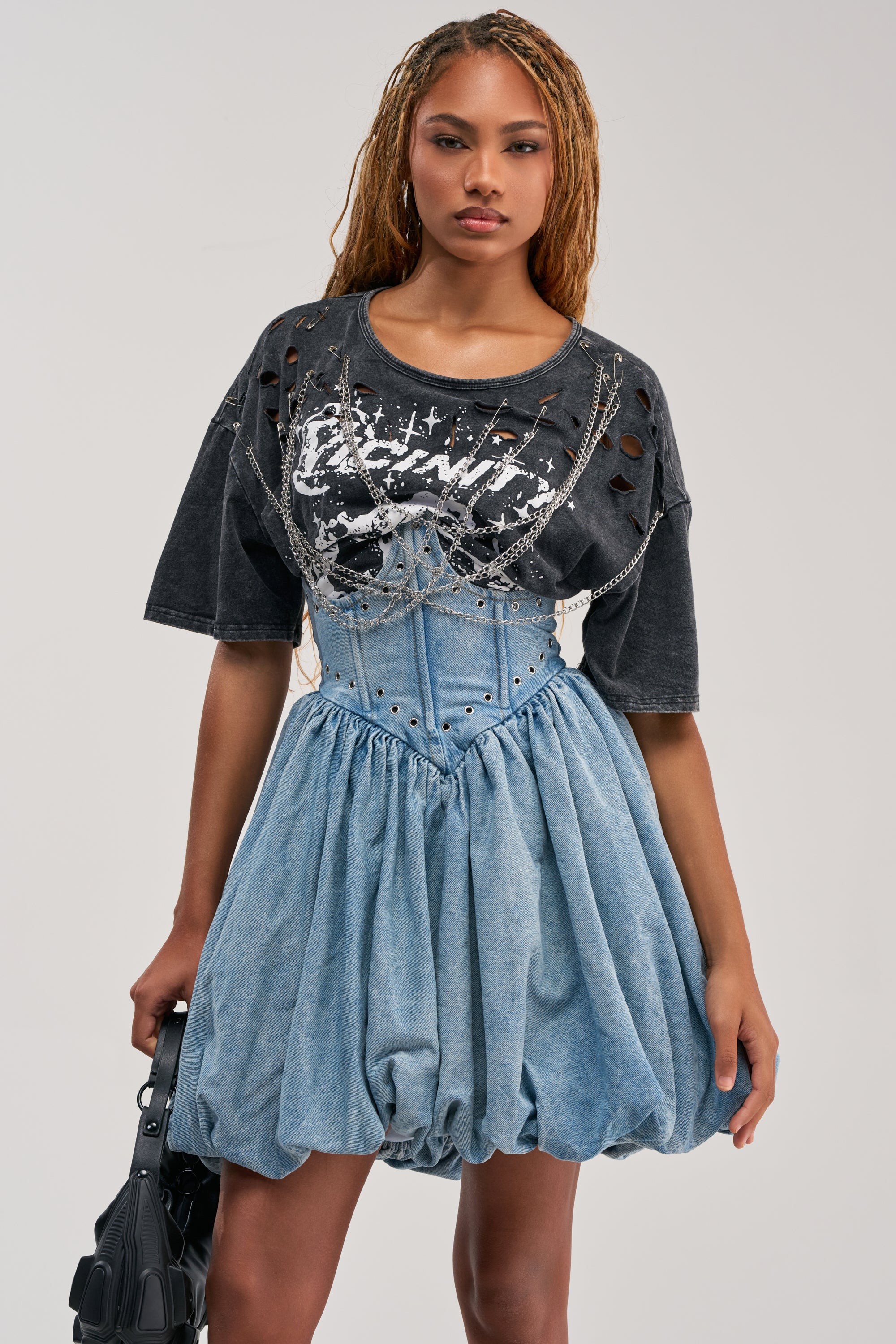 A woman showcases effortless streetwear styling, standing against a plain light background in the COOL GIRLS ONLY MINI DRESS layered over a black graphic t-shirt and accessorized with a black handbag.