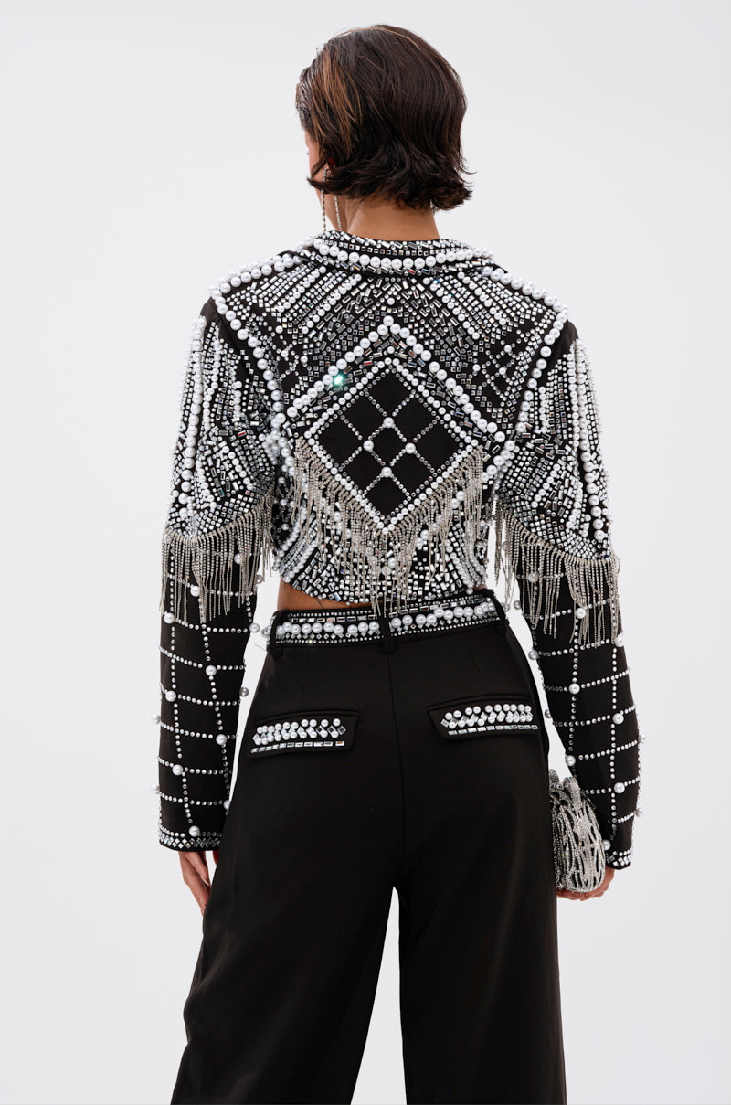 A person with short dark hair, seen from behind, wears the DIRTY MARTINI EMBELLISHED BLAZER with silver beads and geometric patterns, paired with high-waisted black pants featuring beaded embellishments on the pockets.