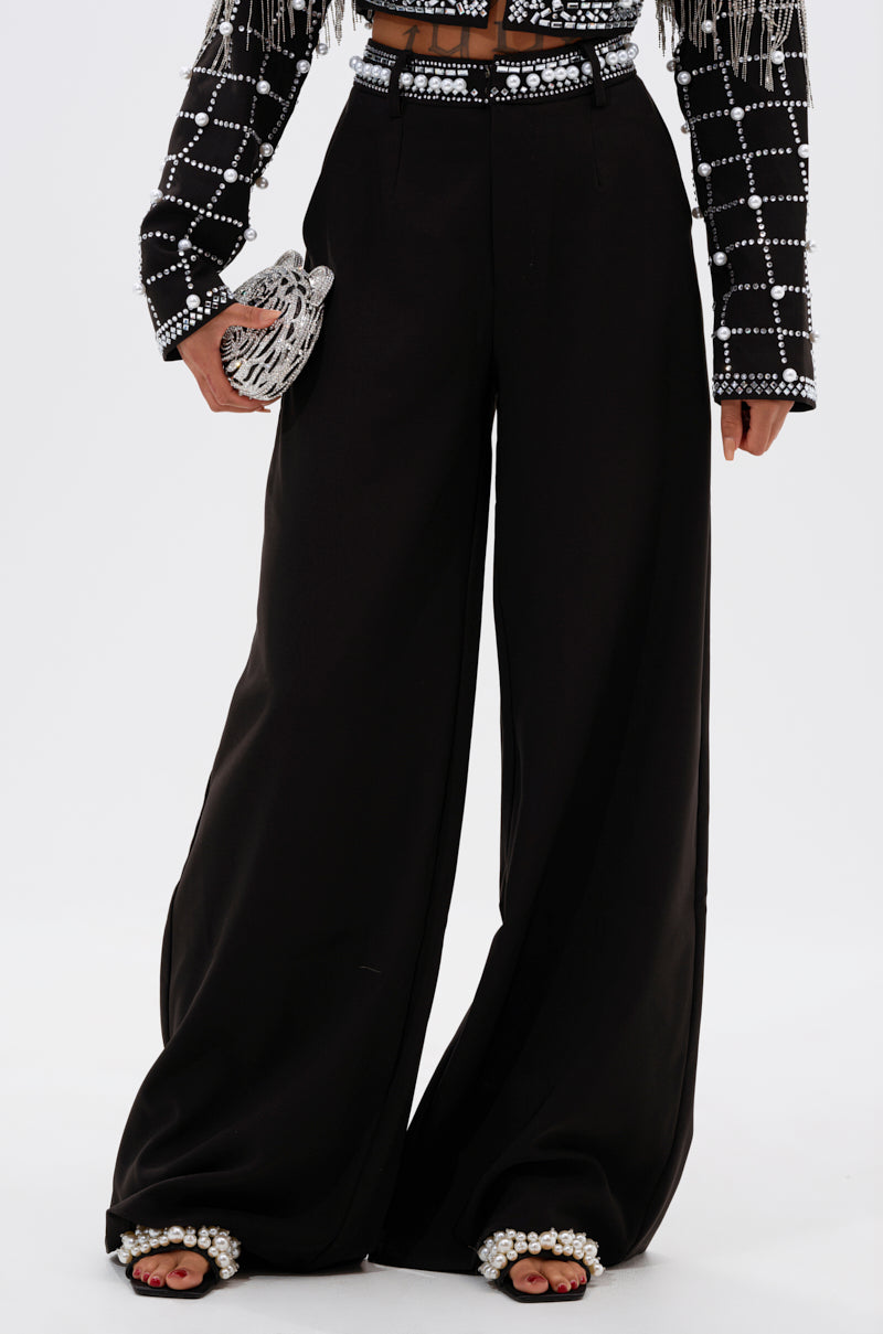 A person wearing DIRTY MARTINI EMBELLISHED TROUSER, a black cropped jacket with silver embellishments, and holding a small silver beaded clutch.