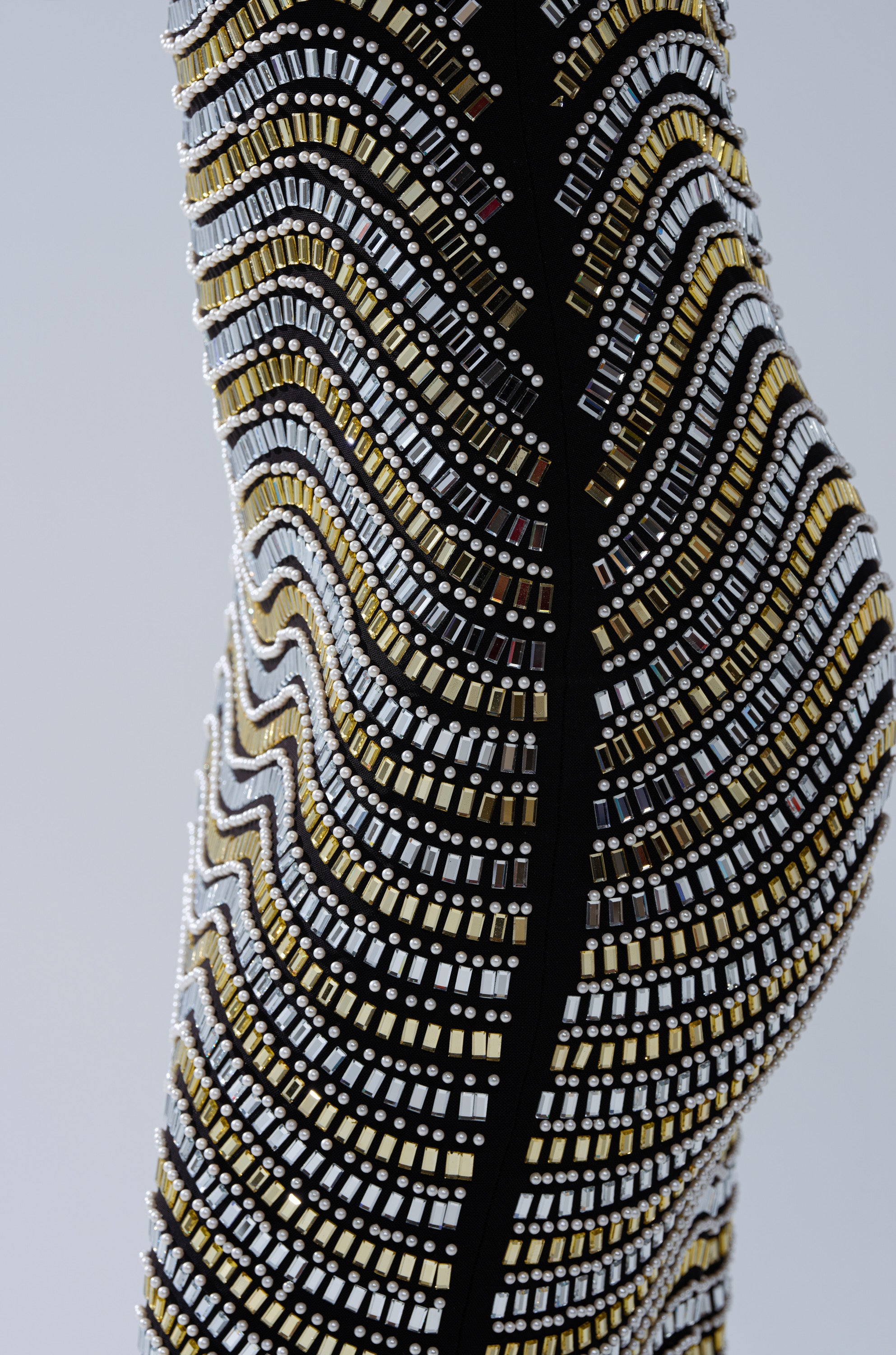 A close-up of the SHINE ON RHINESTONE MIDI DRESS, featuring a fitted mesh design adorned with wavy rows of gold, silver, and black rectangular beads, forming an intricate textured pattern against a pale background.