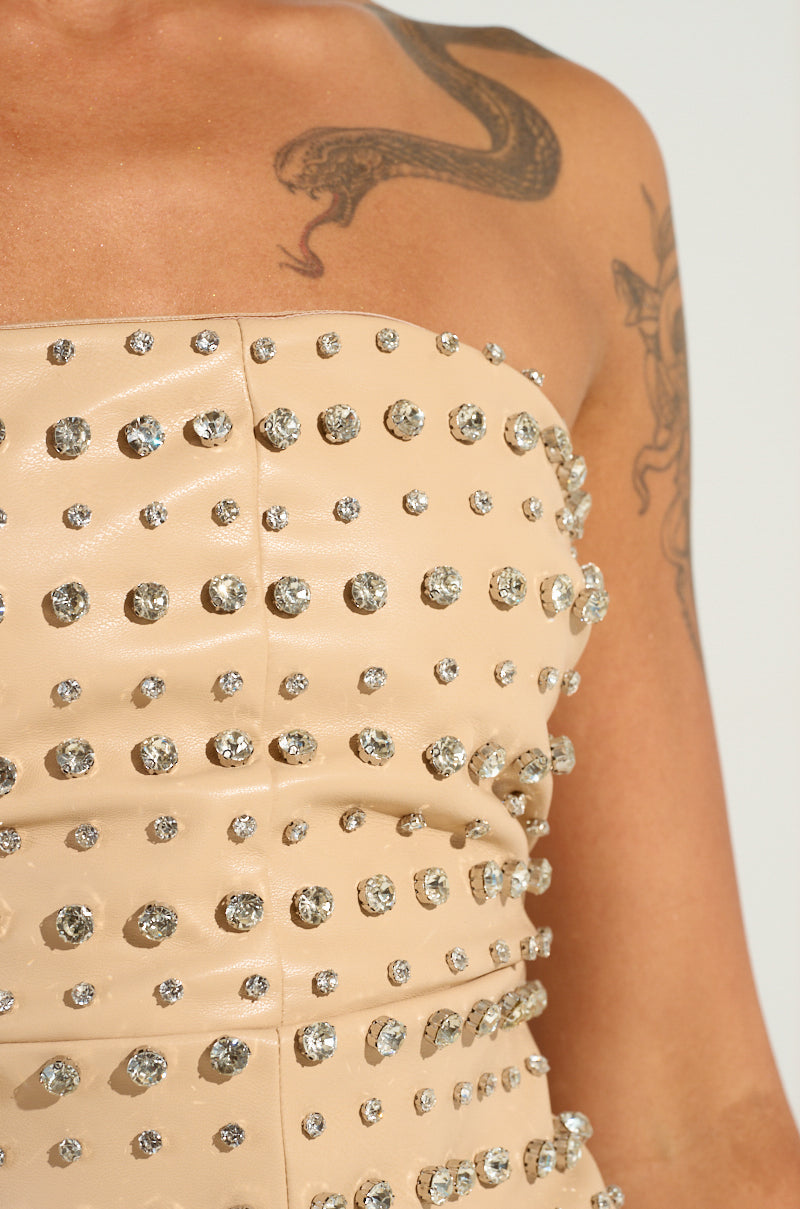 A person wearing a strapless beige dress embellished with silver rhinestones, drawing attention to its intricate detailing that echoes the TELL ME ABOUT IT STUD PU MINI DRESS. The arm and shoulder reveal tattoos, featuring a snake among other designs.
