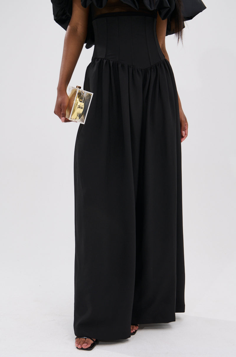 Wearing the BETTER THAN THIS CORSETED TROUSER with a wide-leg silhouette and an off-the-shoulder top, a person holds a small transparent clutch against a plain white background.