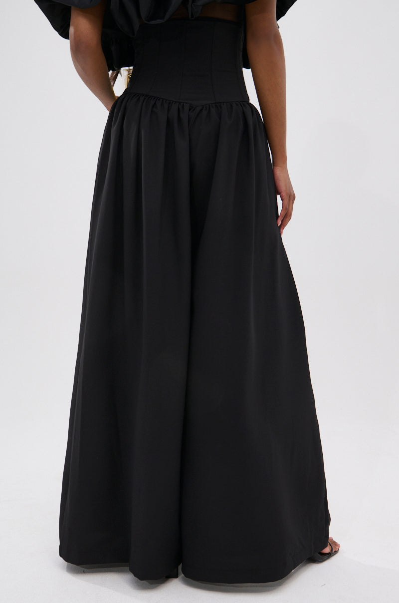 Wearing the BETTER THAN THIS CORSETED TROUSER, a person stands with their back to the camera, showcasing high-waisted, wide-leg black trousers against a plain light background.
