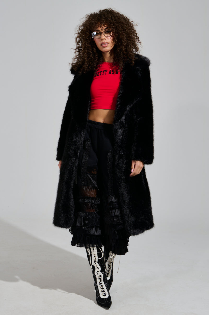 A woman with curly hair confidently poses against a plain background, wearing an ALL OVER THE PLACE PANT, complemented by a red crop top and black fur coat. Her knee-high lace-up boots add the final touch to her stylish ensemble.