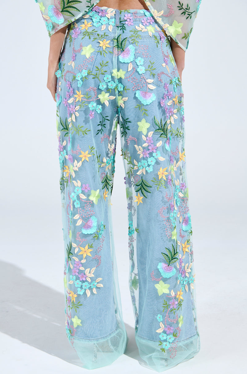 Someone shows off the GARDENIA DENIM WITH FLORAL TULLE WIDE LEG JEANS, sheer blue pants featuring a wide-leg cut and multicolored floral embroidery. The floral tulle overlay adds to the lightweight design, ideal for a stylish spring or summer look. 3