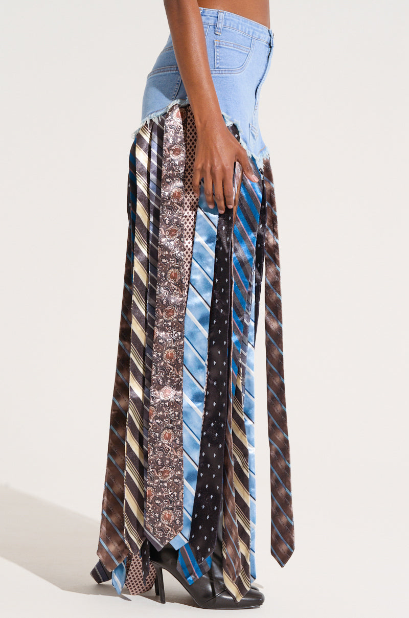 A person is wearing the SO YOU THOUGHT DENIM SKIRT WITH TIE, a maxi-length skirt crafted from various neckties. The ties, featuring an array of patterns and colors like stripes, polka dots, and paisley designs, dangle down to create the skirt. Paired with black shoes, this ensemble offers a unique twist on denim fashion.