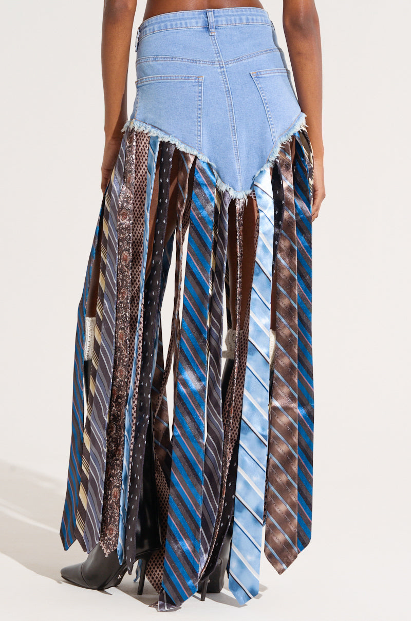 A person wearing the "SO YOU THOUGHT DENIM SKIRT WITH TIE," a unique maxi-length denim skirt featuring a semi-stretchy blue denim upper section adorned with multiple neckties hanging down as tassels. The neckties showcase various patterns, primarily in blue and brown hues. The person is also wearing tall black boots.