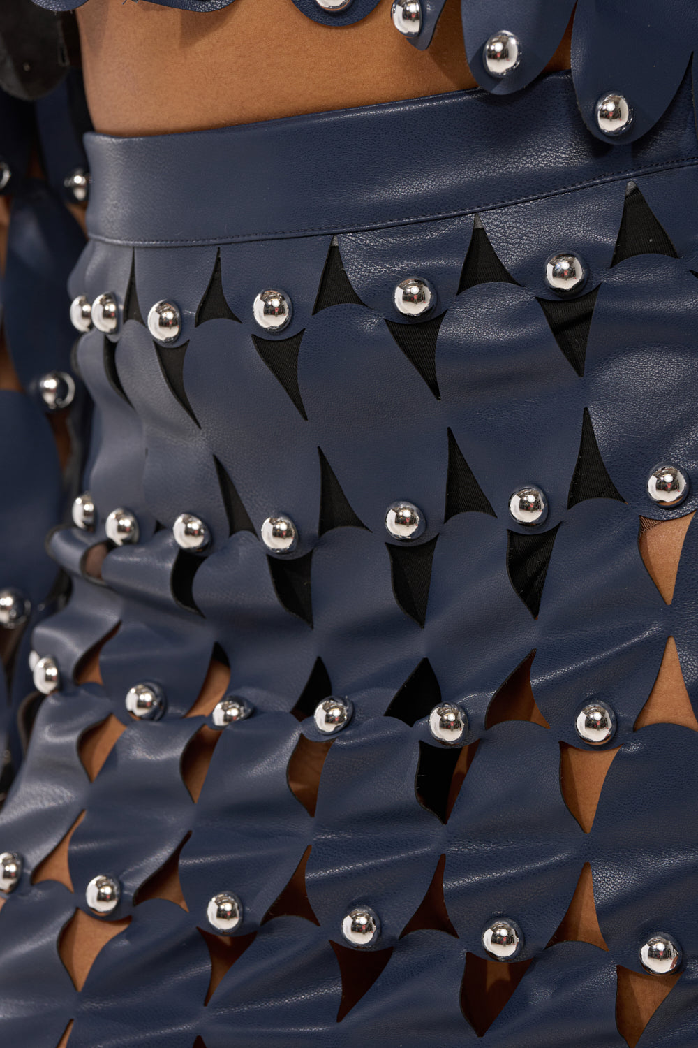 Close-up of THE SNEAK PEEK STUDDED PU MIDI SKIRT IN NAVY, crafted from overlapping faux leather panels with silver studs and black triangular accents for a bold, geometric look. 6
