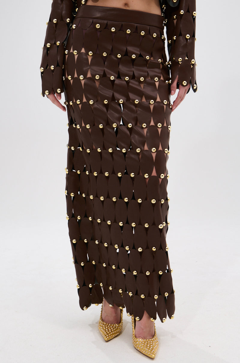 Wearing the SNEAK PEEK STUDDED PU MIDI SKIRT IN BROWN with overlapping oval panels, high-rise waistband, and studded details, the look is finished with matching sleeves and gold-studded pointed heels for a bold statement.