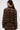 A woman with slicked-back hair is seen from the back wearing the SNEAK PEEK STUDDED PU CROP CARDIGAN IN BROWN, a sheer, long-sleeved top adorned with metallic studs, set against a plain light background.