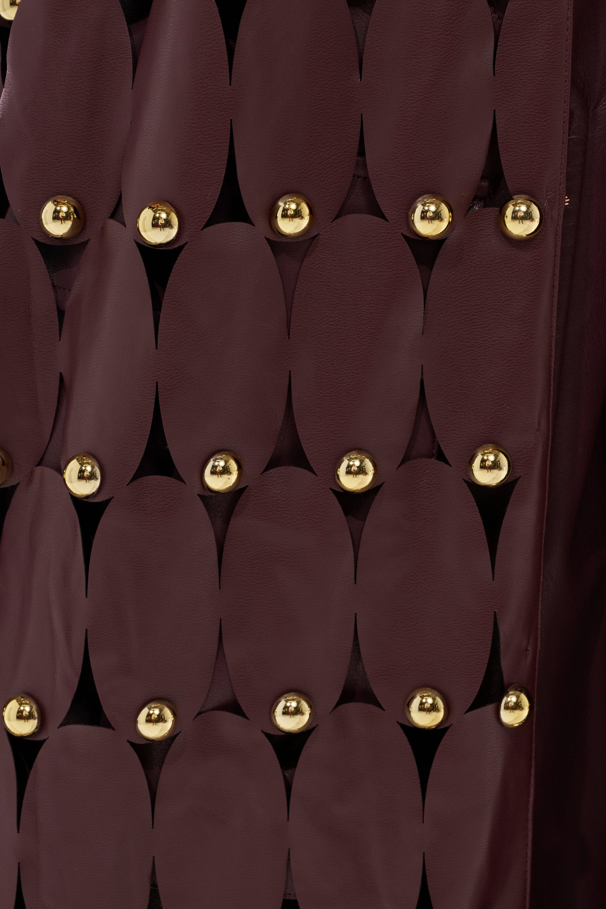 Close-up of THE SNEAK PEEK STUDDED PU LONG CARDIGAN IN BURGUNDY, showcasing oval faux leather pieces joined by metallic studs in a geometric, grid-like pattern.