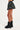 A person is standing on a white background wearing a short, plaid WONDERWALL MINI SKIRT from the AKIRA Label and knee-high black boots with large buckles. The person is shown from the mid-back to their feet, with their legs mostly visible.