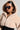 A person wearing the I LIKE IT LIKE THAT ZIP UP HOODIE, a plush, beige faux sherpa hoodie, paired with large sunglasses. They accessorize with a pearl necklace and dangling earrings, looking to the side with a neutral expression against a gray background.