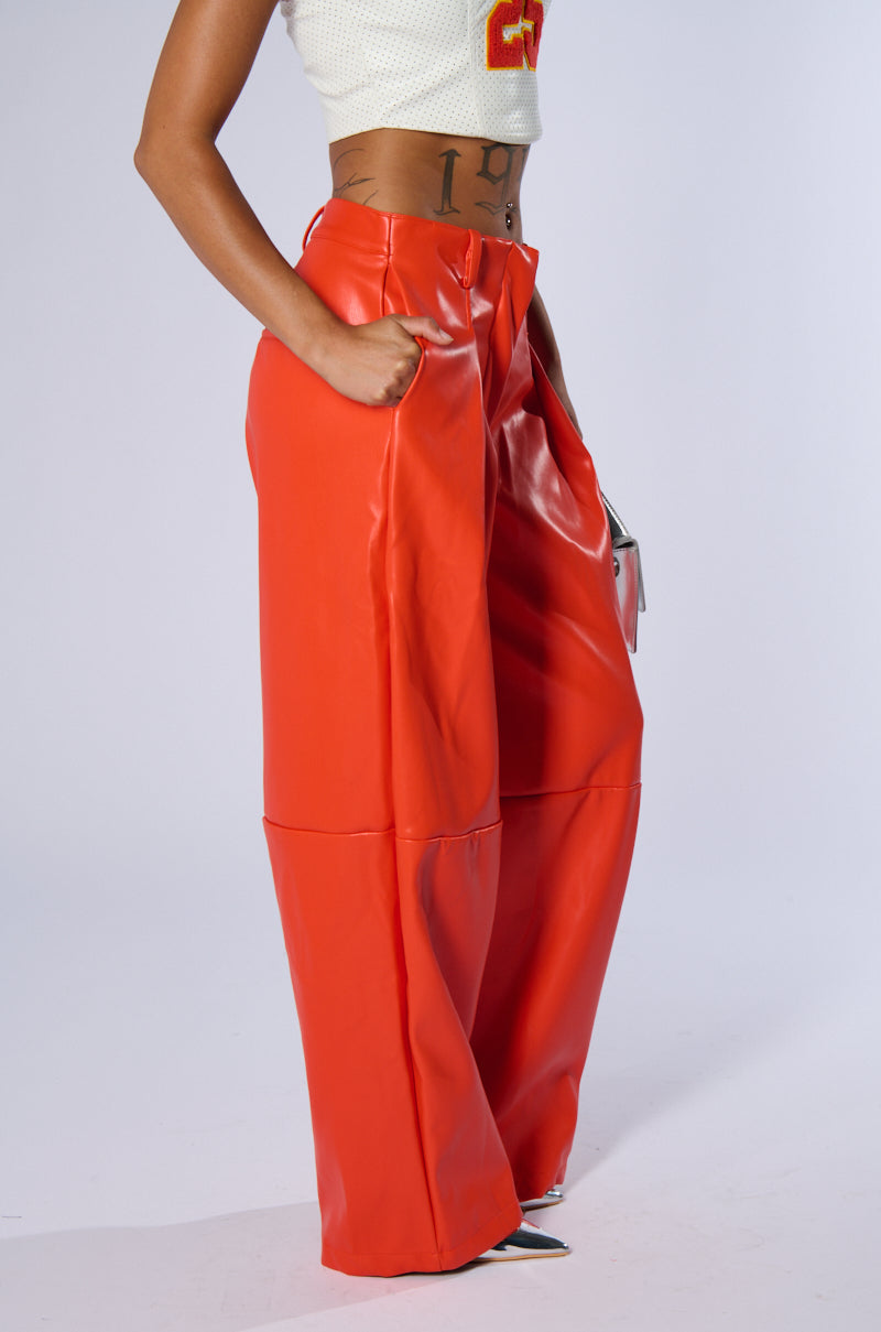 Person wearing BABY COME OVER PU PANT IN ORANGE and a white cropped top, standing with hands in their pockets. The image is cropped above the person's shoulders, focusing on the pants and midsection.