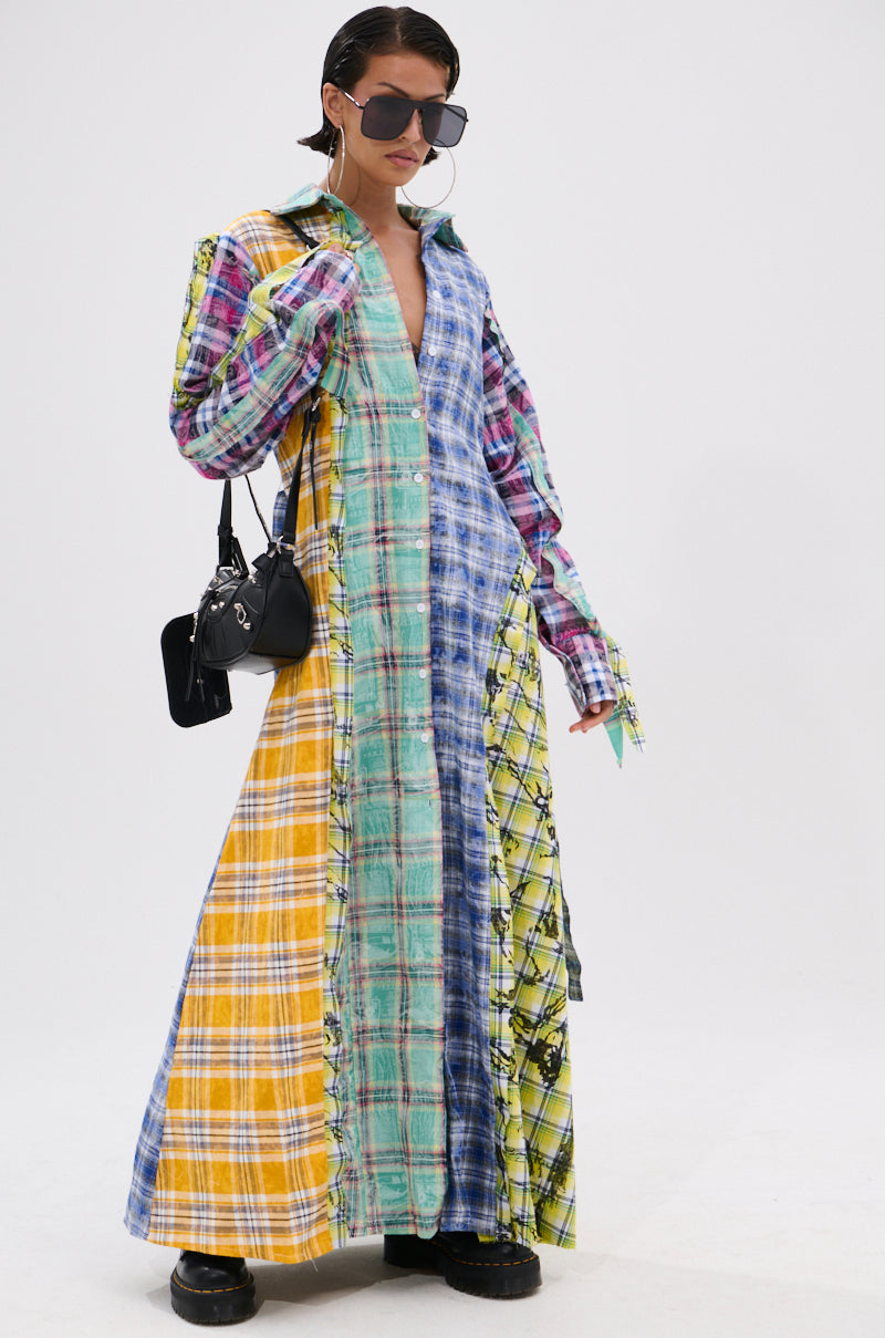 Wearing the STAR OF THE SHOW PLAID MAXI DRESS with a self-tie waist, patchwork in blue, yellow, red, and green, plus black shoes, a black handbag, large sunglasses, and hoop earrings, this person stands against a white background.