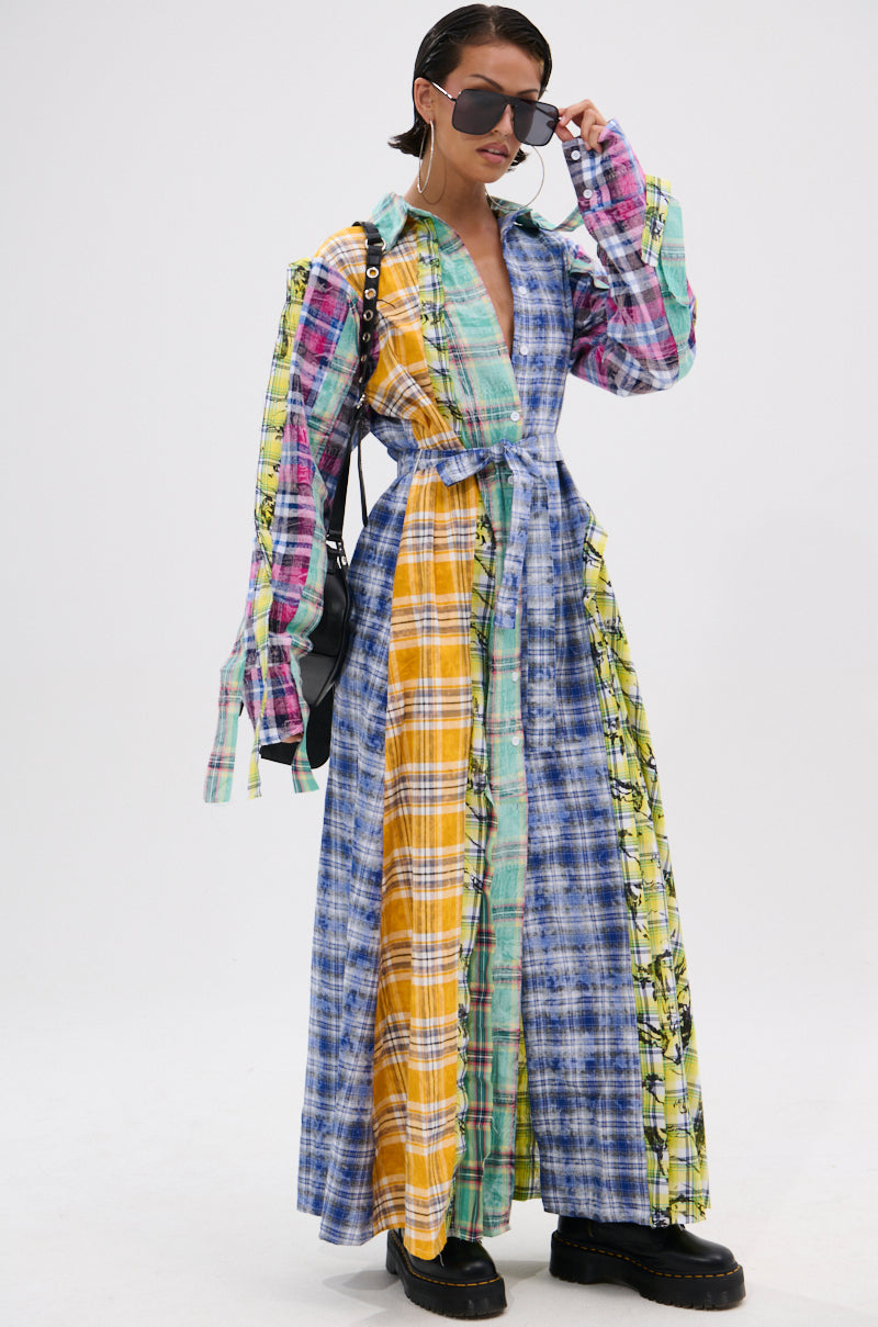 Wearing sunglasses, a person models the STAR OF THE SHOW PLAID MAXI DRESS—with a self-tie waist belt—paired with a black bag and chunky black shoes, posed against a plain white background.