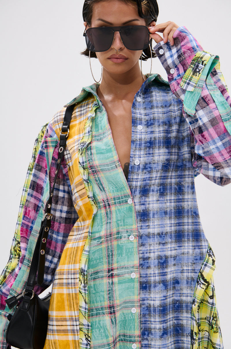 A woman with oversized sunglasses and hoop earrings models the STAR OF THE SHOW PLAID MAXI DRESS in vibrant blue, green, yellow, and pink patchwork plaid. She carries a black purse and exudes confidence.