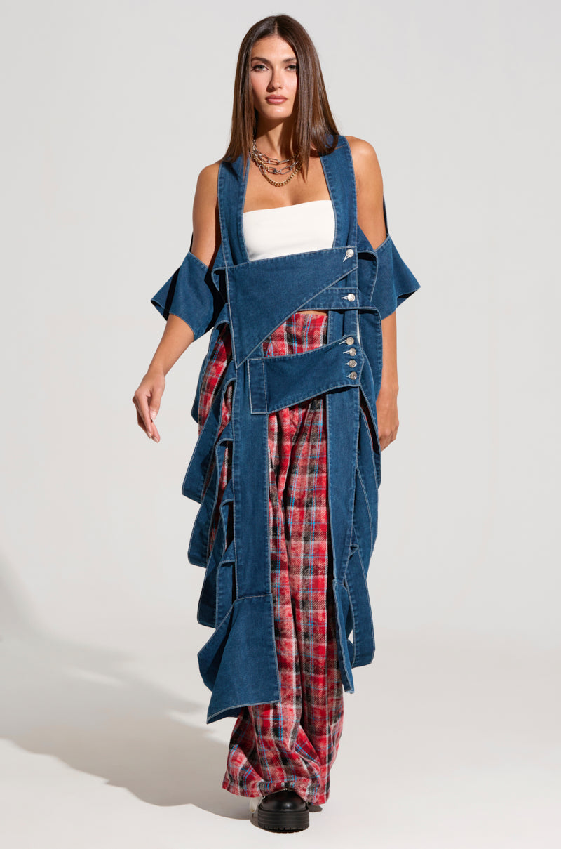 A woman with long brown hair models an eclectic outfit featuring a white tube top, the GEO CUTOUT DENIM DUSTER with distinctive cut-out shoulders, and red plaid wide-leg pants. She completes her look with black platform shoes and multiple necklaces, posing against a plain light grey background.