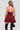 A person with wavy hair holds a small black handbag while wearing the STYLE AND GRACE POPLIN MINI DRESS, a burgundy halter dress with a corset-inspired bodice, paired with black lace thigh-high stockings. The flouncy skirt of the dress elegantly flares out at the bottom against a plain, light-colored background.