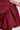 Close-up of a person wearing the STYLE AND GRACE POPLIN MINI DRESS in a wine color, showcasing its flouncy skirt with a gathered, voluminous design on one side. A hand gently touches the fabric, highlighting the texture and folds.