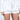 The individual is wearing the BETSY BLOOMER SHORT IN WHITE, high-waisted satin with ruffled edges, paired with a matching long-sleeved white ribbed crop top and holding a beaded handbag.