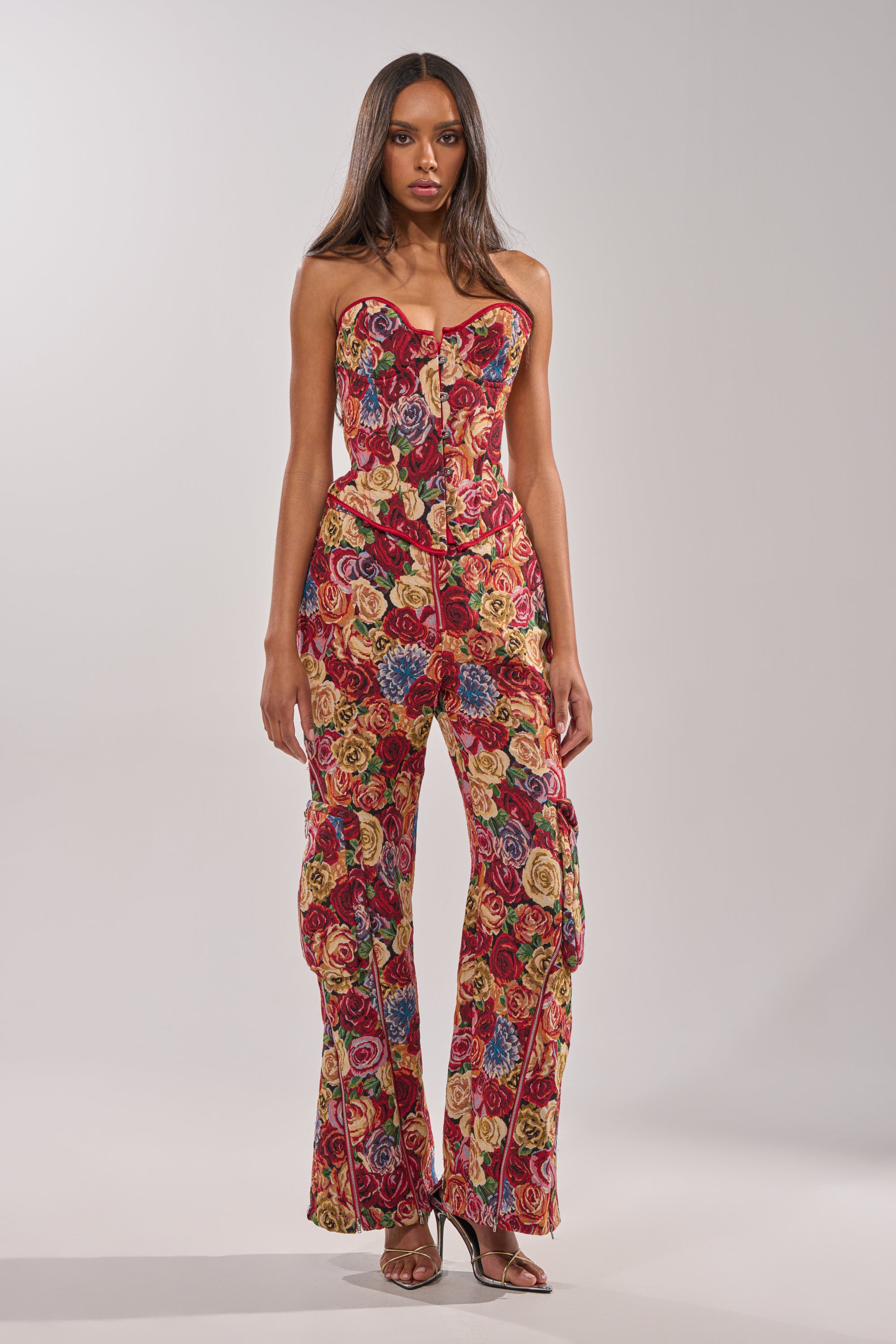 A woman with long hair poses neutrally against a light gray background, wearing the INTO THE THICK OF IT FLORAL BROCADE CORSET—a strapless, form-fitting piece featuring a vibrant multicolored floral pattern. 4