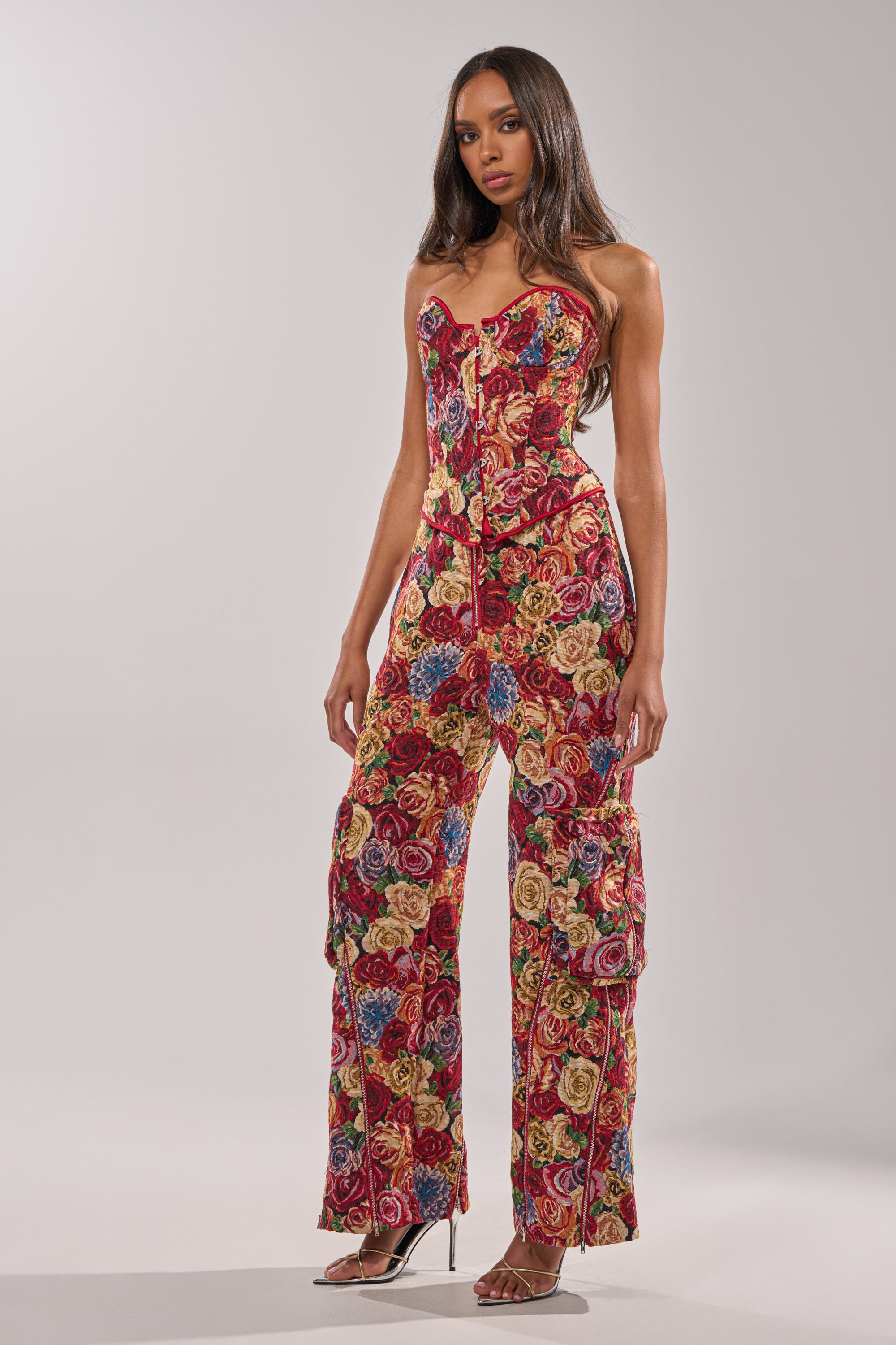 A woman wears the INTO THE THICK OF IT FLORAL BROCADE CORSET and wide-leg printed pants with clear high-heeled sandals, standing against a plain light background. 5