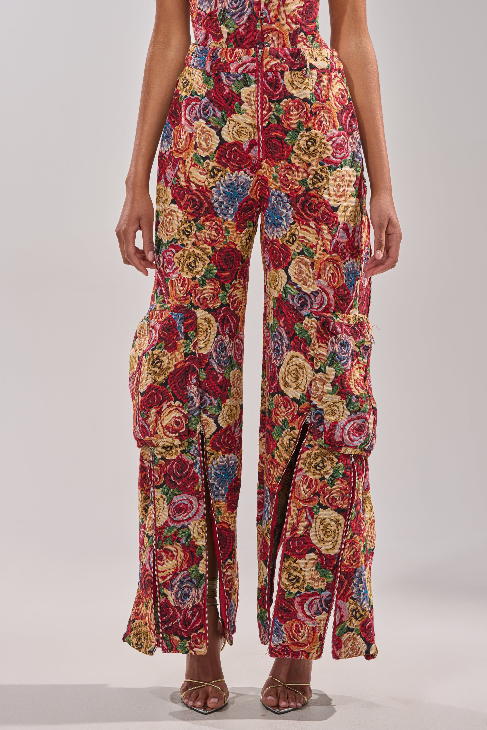 Wearing the INTO THE THICK OF IT FLORAL CARGO PANT—high-waisted, wide-leg with floral tapestry, large cargo pockets, and front slits—paired with open-toed heels. 0