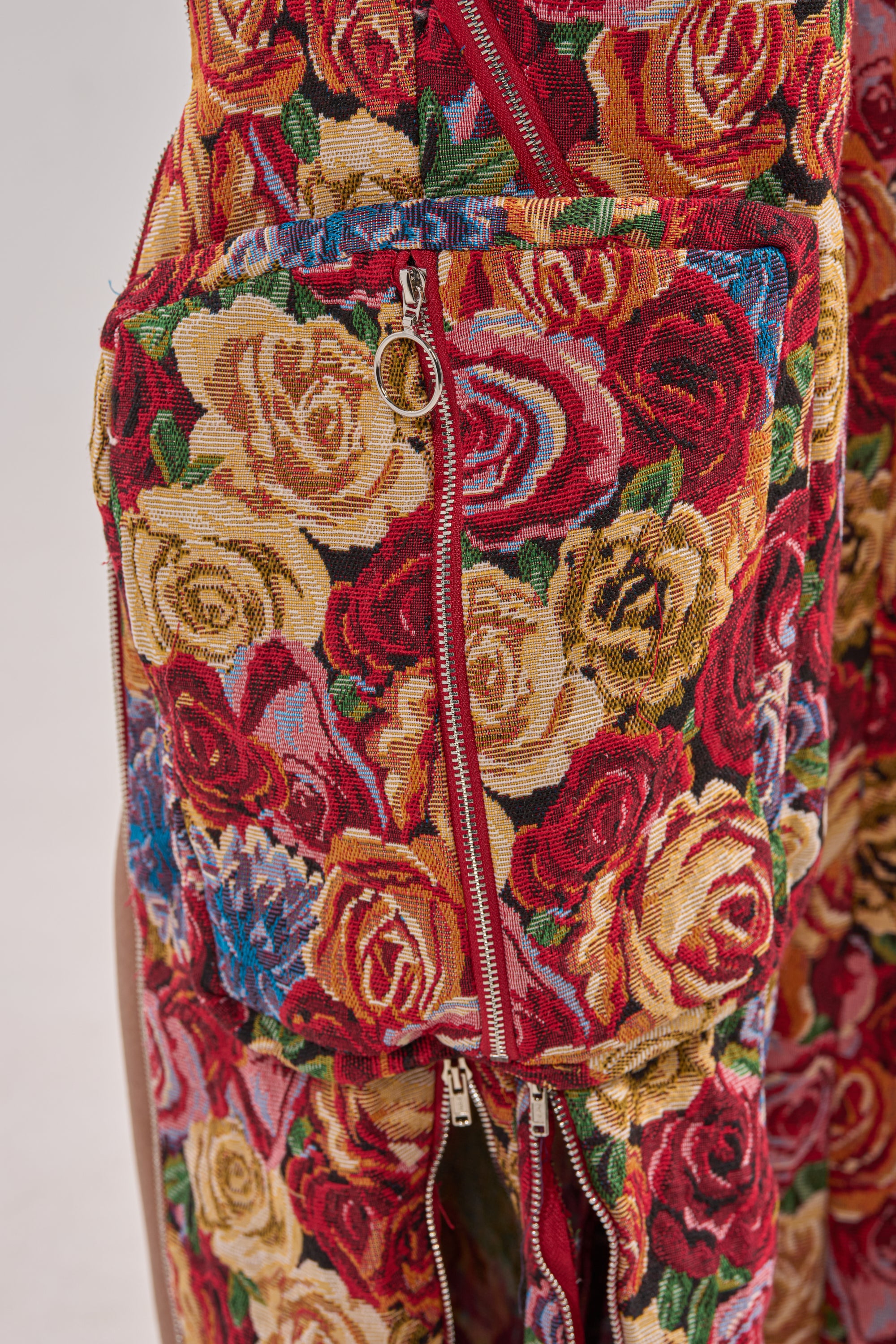 Close-up of INTO THE THICK OF IT FLORAL CARGO PANT with a colorful vintage-inspired rose print in red, yellow, and pink. Features multiple zippered pockets with gold-tone pulls for added style and function. 11