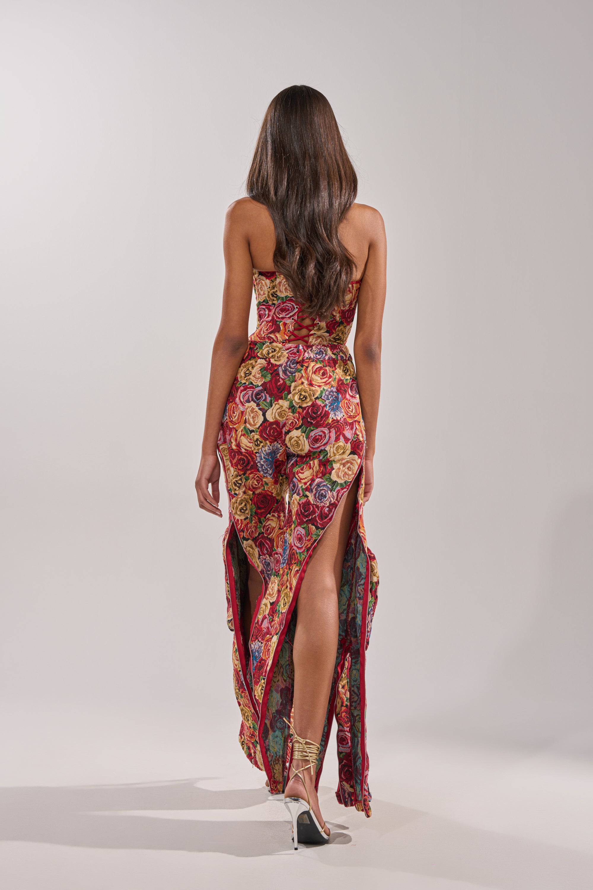 A woman with long brown hair is seen from behind, wearing the INTO THE THICK OF IT FLORAL CARGO PANT and strappy high heels, standing against a plain light background. 6