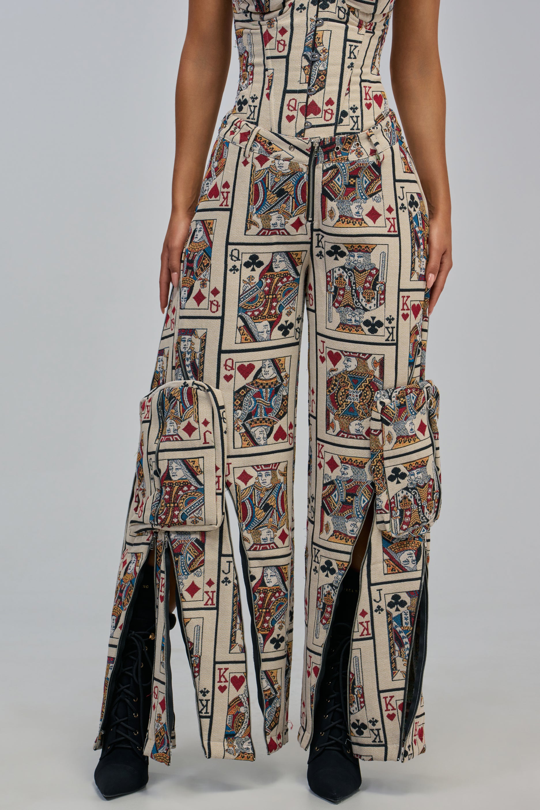 Wearing the WIN ME SOME MONEY CARGO PANT in a high-rise, wide-leg fit with large pockets, paired with a matching brocade playing card print top featuring kings and queens. Black lace-up boots complete the bold streetwear look against a plain gray background.