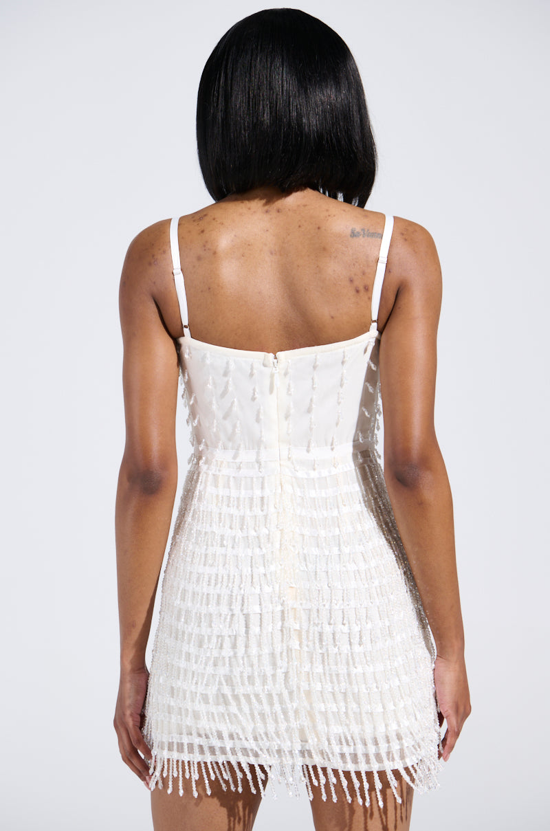 Rear view of a person with short black hair in the SHOW STOPPER BEADED MINI DRESS, featuring fringe details and adjustable straps. Tattoos adorn their upper back as they stand against a plain white background.