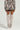 A person dressed in a FLOWER CHILD PRINTED MINI SKIRT paired with a matching floral camo outfit and thigh-high beige boots stands facing away. The slouched design of the boots enhances their style against a plain background.