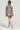 Dressed in the AKIRA Label FLOWER CHILD PRINTED MINI SKIRT, a woman exudes confidence with her floral camo outfit. The mini skirt, embellished with pink rose patterns, is perfectly complemented by a matching jacket, sleek sunglasses, statement earrings, and knee-high beige boots.