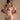Wearing the LA LA LOVE ME SATIN ROMPER, a light pink off-the-shoulder satin romper with short puff sleeves and a matching neck ribbon, a woman stands against a neutral background, gazing slightly to the side.
