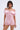 A woman models the LA LA LOVE ME SATIN ROMPER, featuring a shiny light pink satin fabric, V-neckline, and short puff sleeves. She stands against a plain light background, looking at the camera.