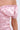 A close-up of a person wearing the LA LA LOVE ME SATIN ROMPER, featuring light pink satin fabric, off-the-shoulder design, ruching, and short puff sleeves that highlight its elegant shine and stylish texture.