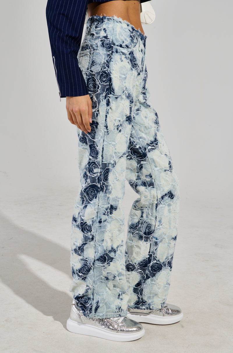 Someone is rocking the "TOO COOL FOR YOU DENIM PANT" in a tie-dye pattern with rose designs, featuring a high-rise and wide-leg silhouette, paired with glittery silver sneakers. They're also wearing a dark pinstriped jacket, but their face stays obscured — truly embodying the "Too Cool For You Denim" aura.