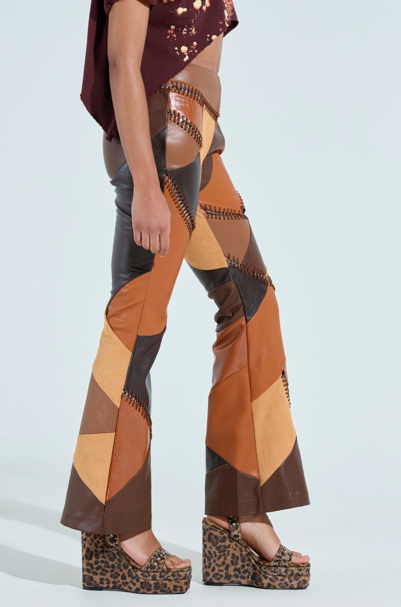 Someone wears the TALK LATER PATCH FAUX LEATHER FLARE PANT in shades of brown and tan, featuring a high-rise fit and flared legs, paired with leopard print platform sandals. The look is completed with stitching details and a floral-patterned cropped top against a light background. 4