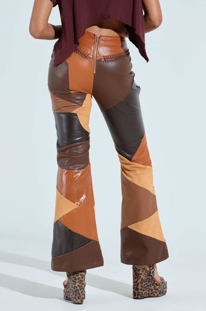 A person wearing the TALK LATER PATCH FAUX LEATHER FLARE PANT with a high-waisted, patchwork design and flared leg silhouette in brown and tan shades, paired with leopard print platform shoes. The top is a cropped maroon shirt. The photo is shot from the back. 5