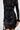 The individual is clad in a black lace dress accented by the COQUETTE COUTURE BOW BELT, which adds a satin corset-inspired touch with charming ribbon details. The outfit is enhanced by lace sleeves and hem, while they carry a black handbag in one hand to round off the sophisticated look.
