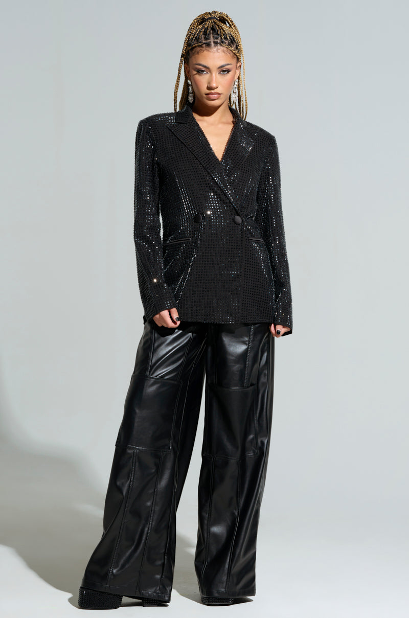 A person with blonde braids stands confidently, showcasing the BOTTOMS UP EMBELLISHED BLAZER and wide-leg black leather pants that seamlessly transition from office to party, all set against a plain background.