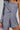 A person wearing the OUT OF OFFICE BLAZER ROMPER, a stylish, business-chic asymmetrical gray romper that resembles a blazer with its single long sleeve and button details. The textured fabric provides a modern, tailored look set against a plain background.