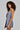 Against a plain background, a person with curly hair radiates business-chic elegance in the OUT OF OFFICE BLAZER ROMPER. This ensemble showcases an asymmetrical design with button detail on one side, and is perfectly accessorized with a silver necklace, adding just the right touch of sophistication.