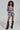 A person with curly hair presents a business-chic look, effortlessly draping the *OUT OF OFFICE BLAZER ROMPER* over one shoulder. The ensemble is beautifully completed with knee-high black boots embellished with silver chains.