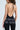 A person with curly hair is wearing a backless black AKIRA Label jumpsuit, glittery text on the back reads "HOTTEST TITS ON THE INTERNET." Their super stretchy seamless outfit is complemented by a shiny silver purse.